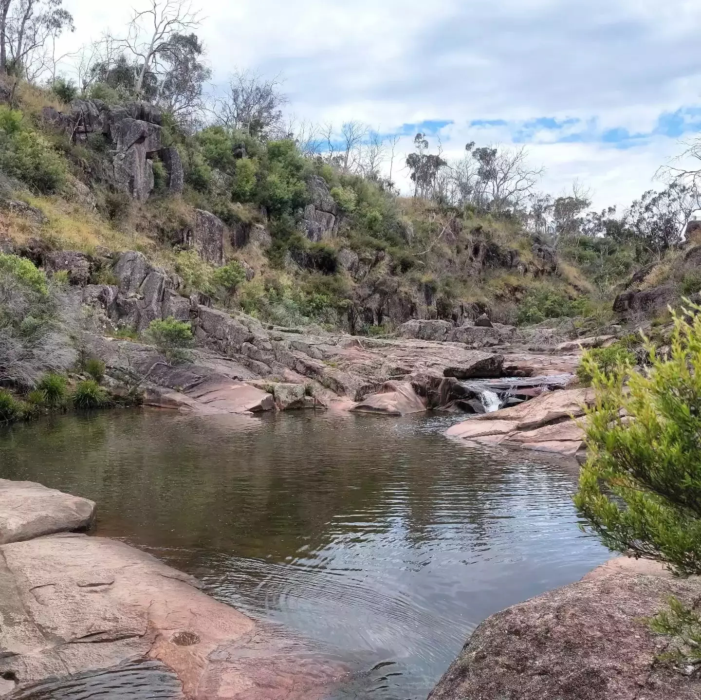 Auto-generated description: A tranquil natural scene features a small waterfall flowing into a rocky creek surrounded by lush greenery and hills.
