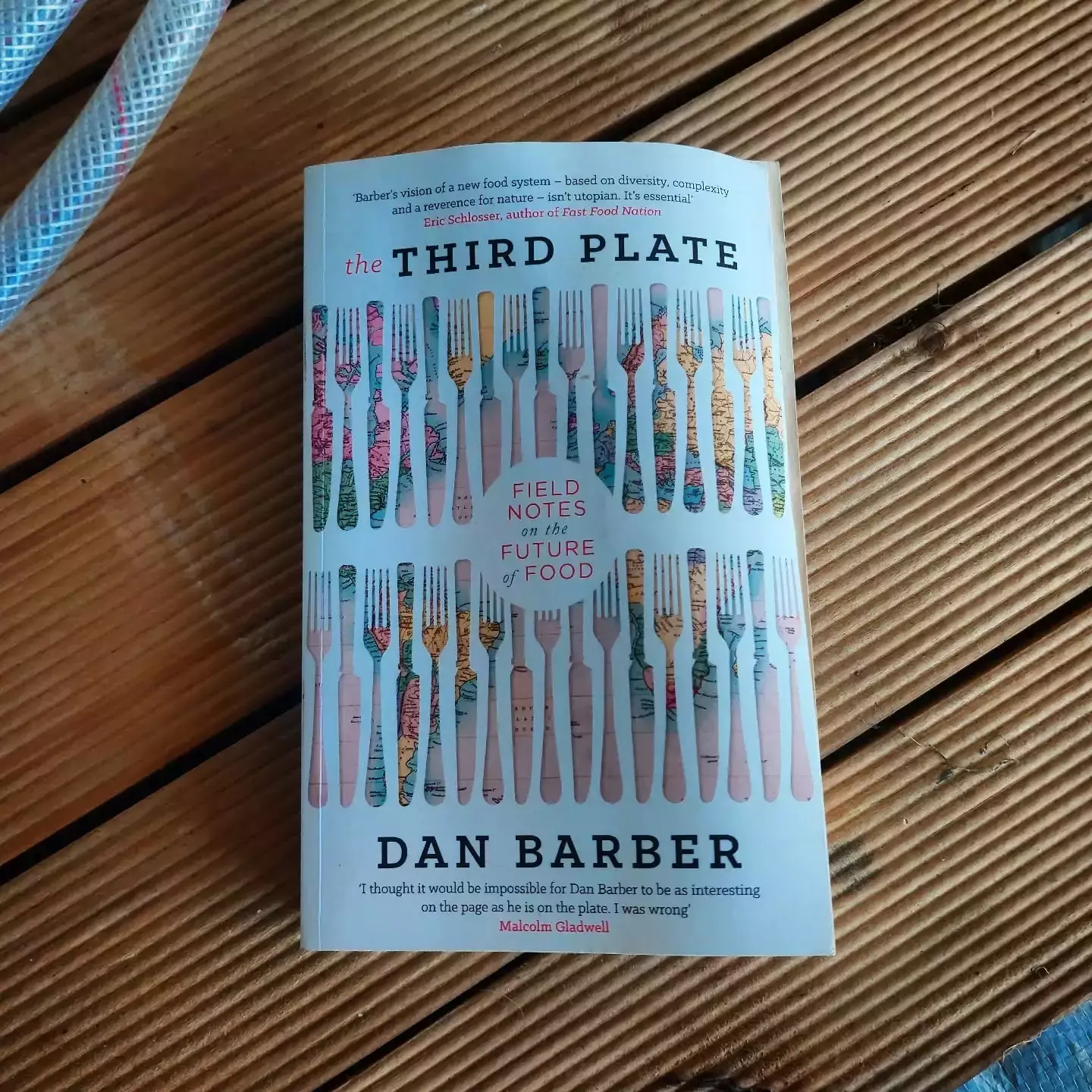 Auto-generated description: A book titled The Third Plate by Dan Barber is placed on a wooden surface next to a coiled rope.