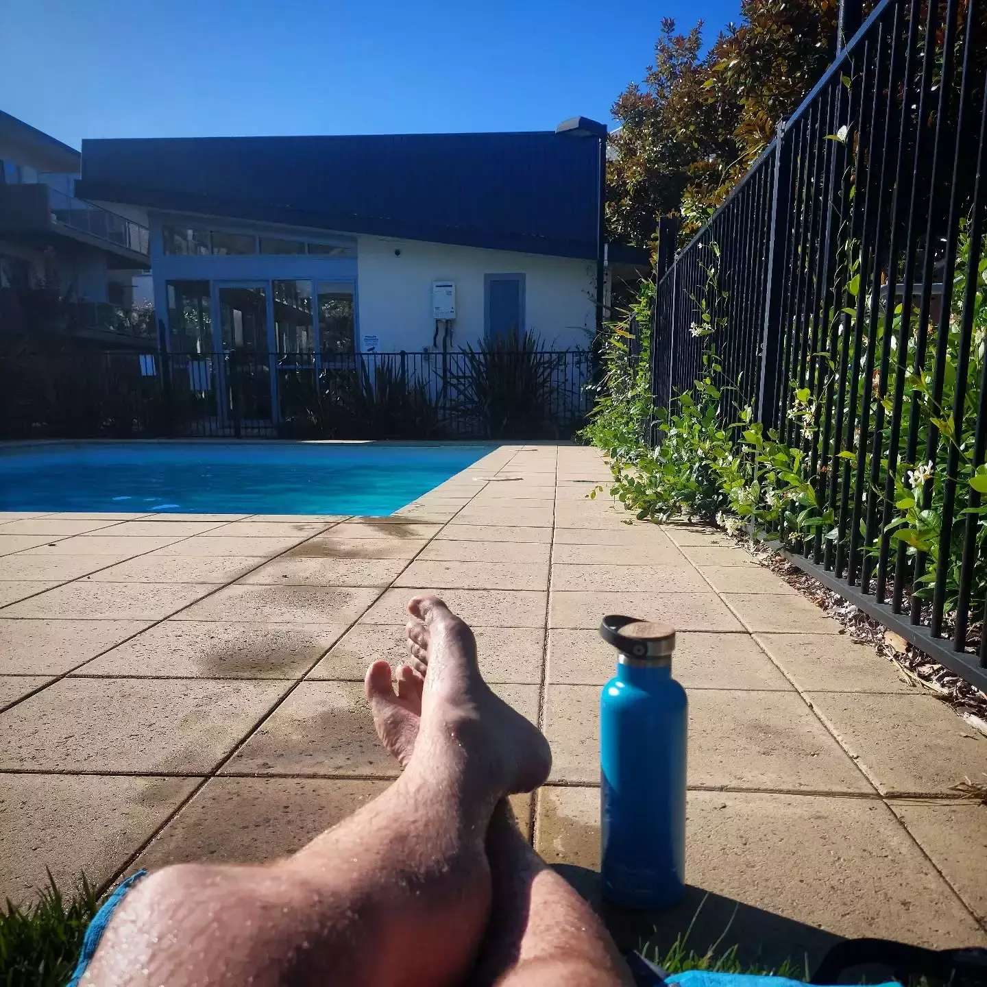 Auto-generated description: A person is relaxing by a swimming pool with a blue water bottle nearby on a sunny day.
