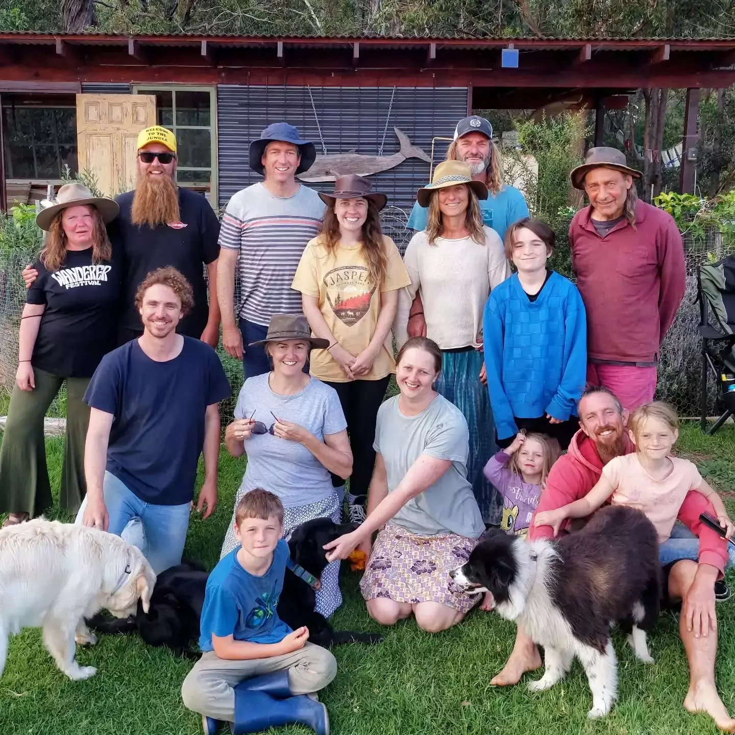 Auto-generated description: A group of people, including adults and children, are posing outdoors with two dogs on a grassy area.