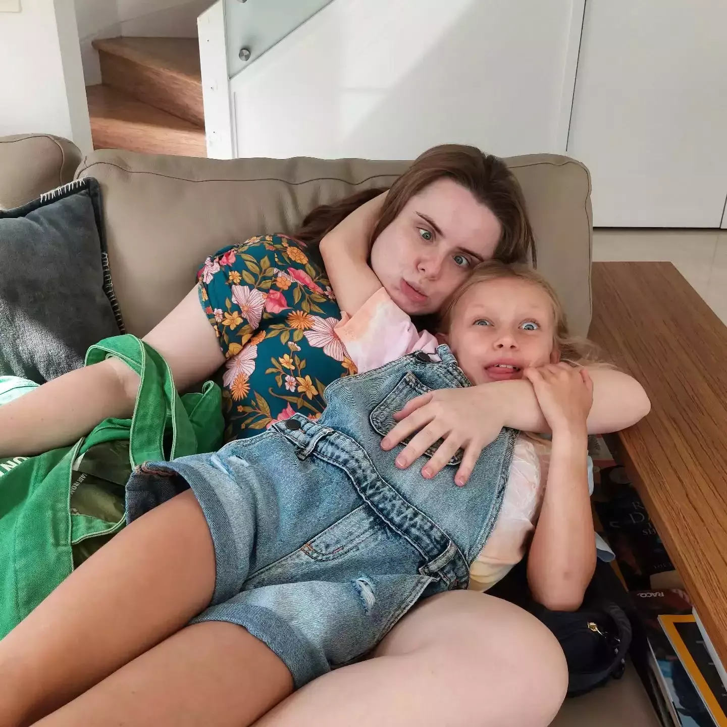 Auto-generated description: A person with a surprised expression is lying on a couch, embracing a child who also looks surprised.