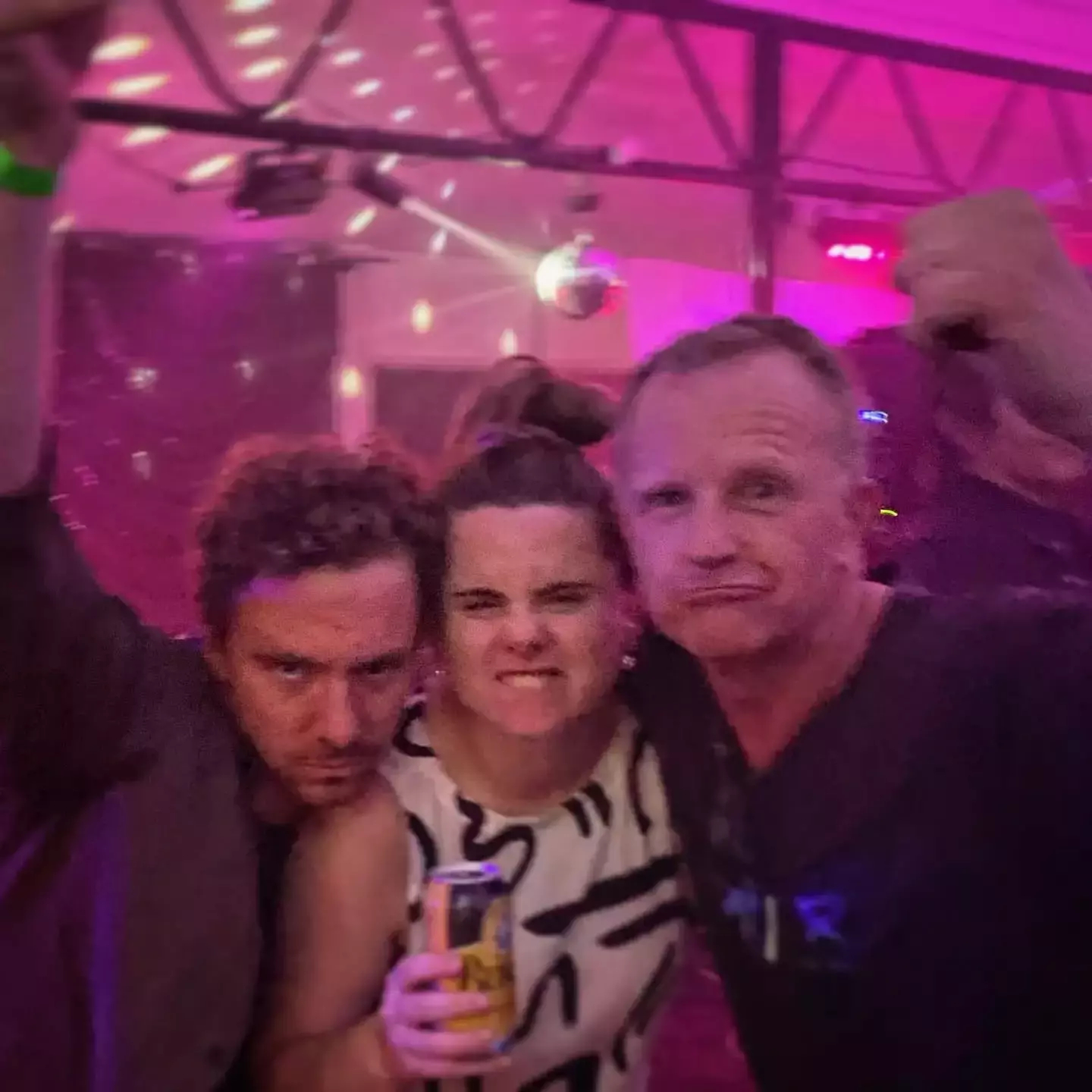 Auto-generated description: A group of three people posing energetically at a party, with one holding a can.