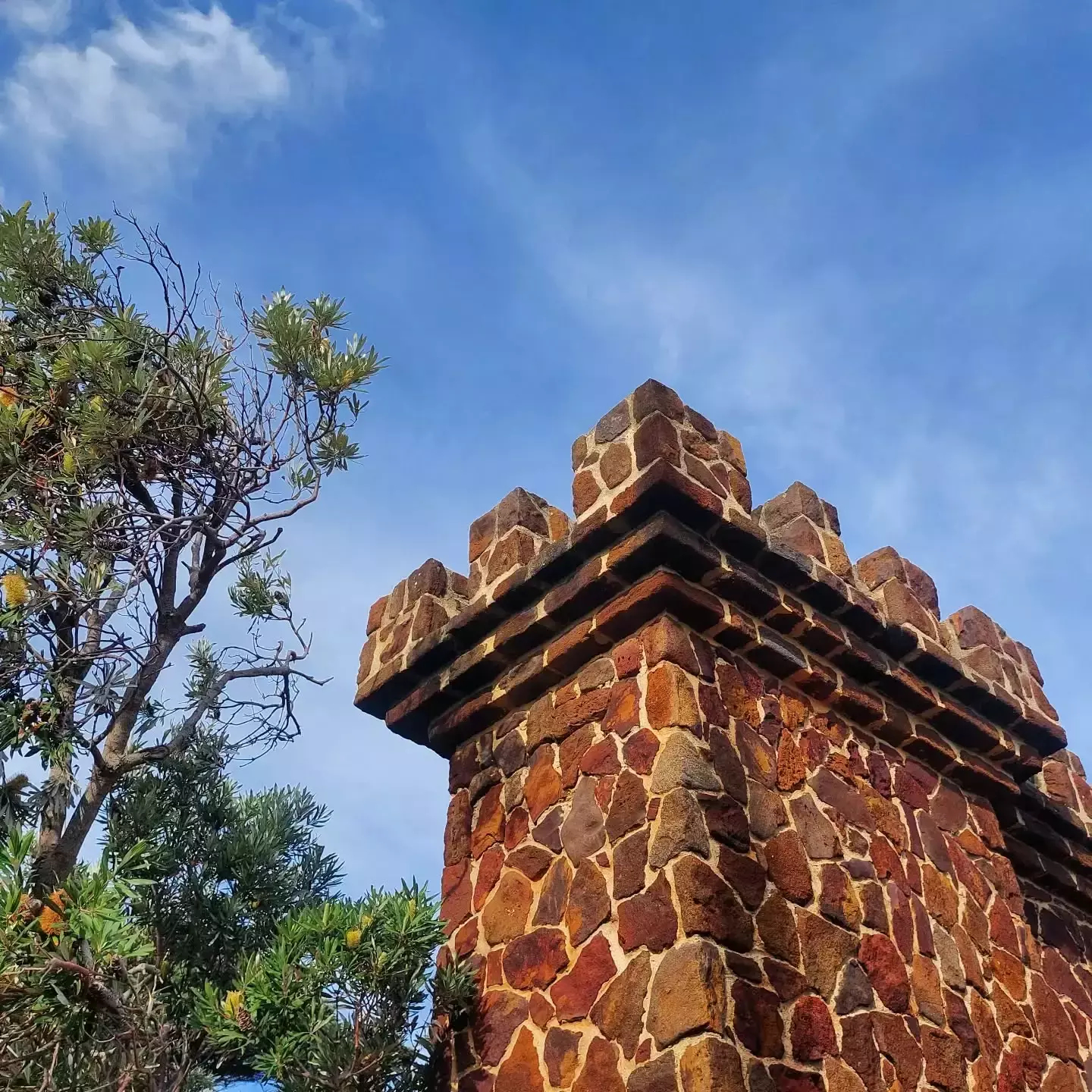 Auto-generated description: A stone tower set against a blue sky is framed by a tree on the left.