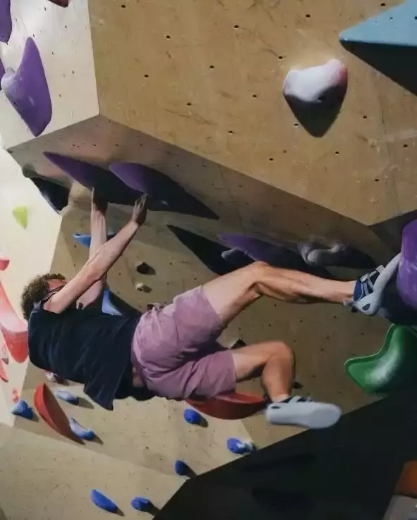Auto-generated description: Joe is bouldering on an indoor climbing wall with various colored holds.