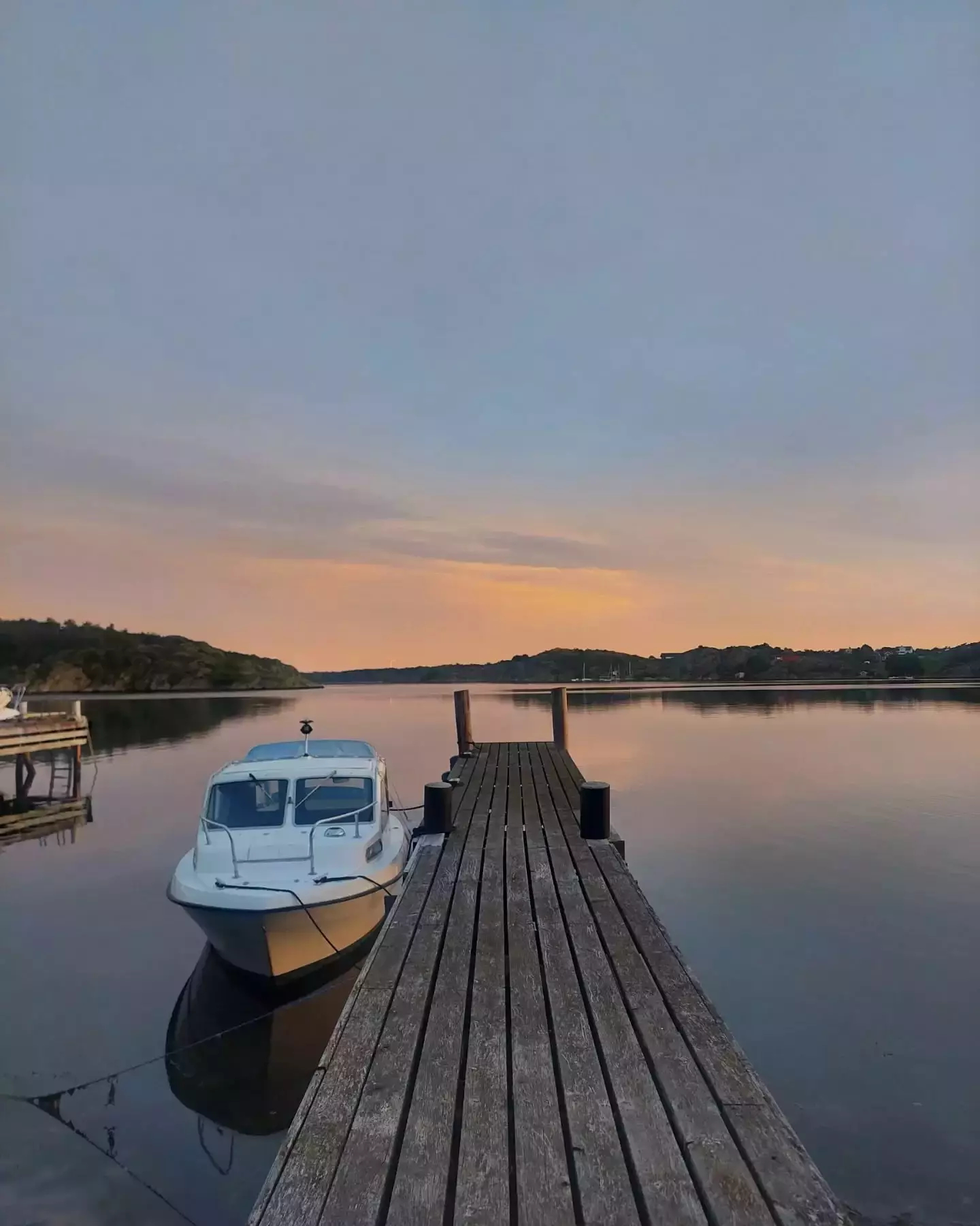 Auto-generated description: A small boat is moored to a wooden dock extending over a calm lake, with a serene sunset in the background.