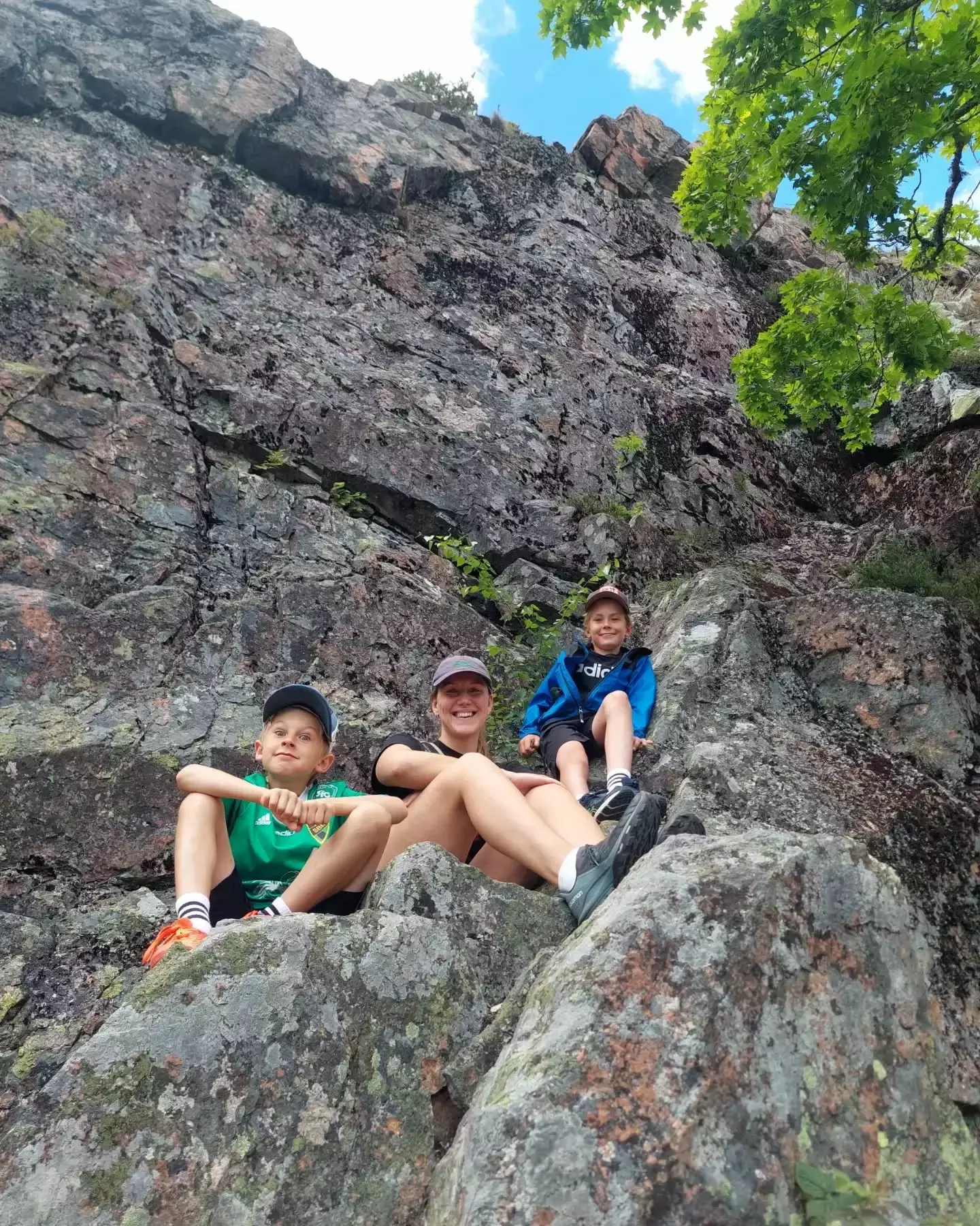 Auto-generated description: Tanjs and her cousins are sitting on a rocky surface under a tree.