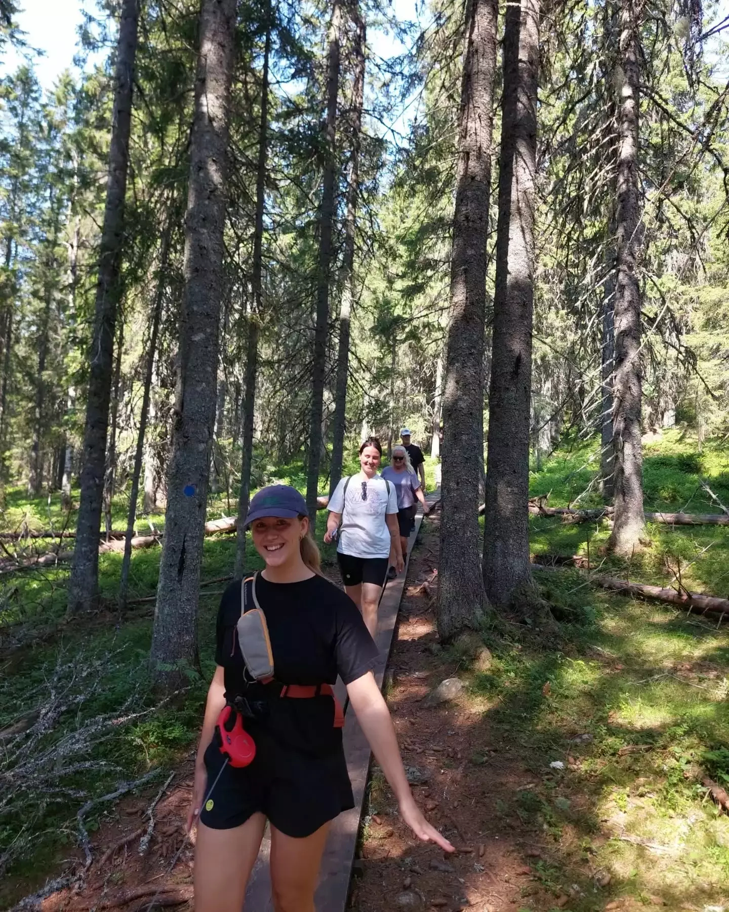 Auto-generated description: Walking with Tanja's faily along a narrow trail in a sunny forest.