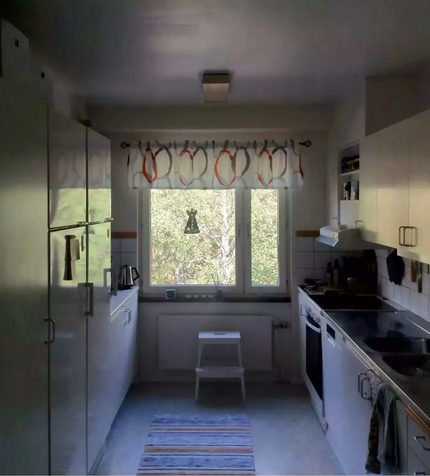 Auto-generated description: A kitchen with white cabinets, a central window adorned with a patterned valance, and various kitchen appliances.
