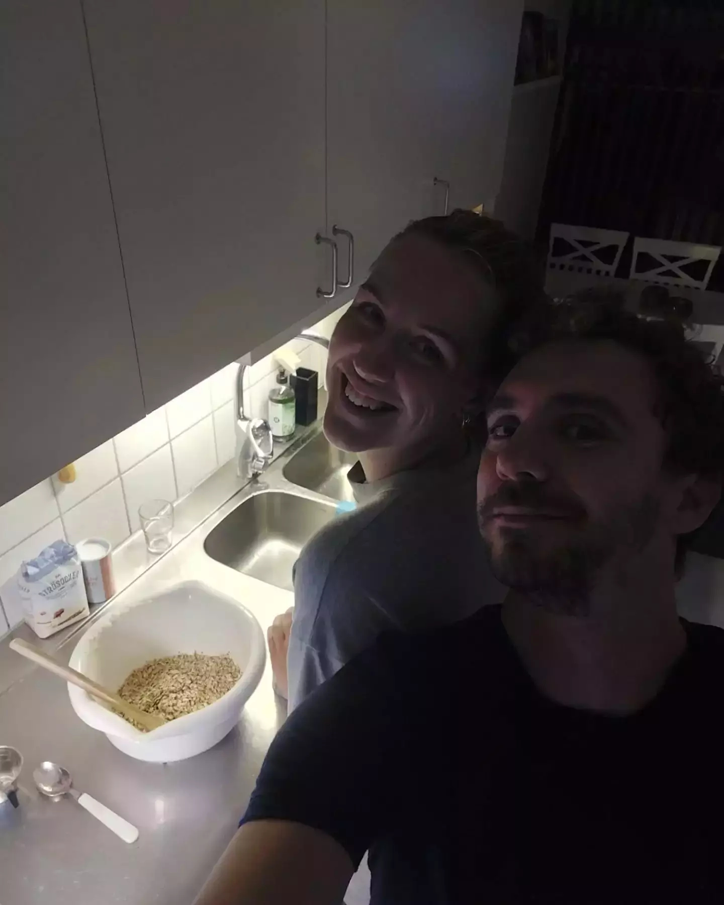 Auto-generated description: Two people are smiling near a kitchen counter with a large bowl of oats.