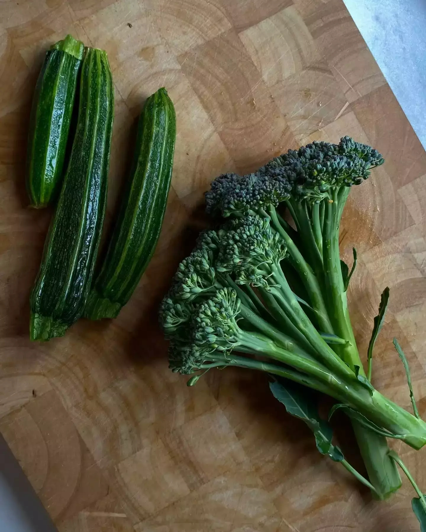 Auto-generated description: Zucchinis and broccoli are placed on a wooden cutting board.