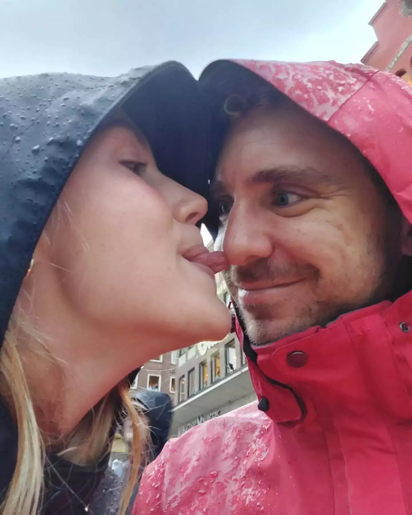 Auto-generated description: Two people wearing hooded rain jackets share a playful moment in the rain.